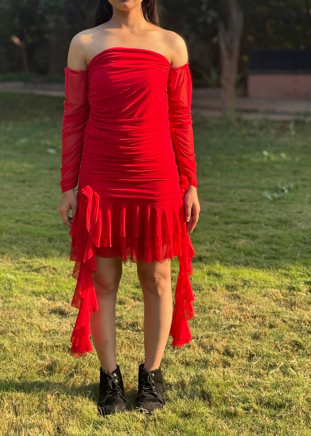 Woman wearing red off-shoulder ruched dress with ruffled hem standing on grass