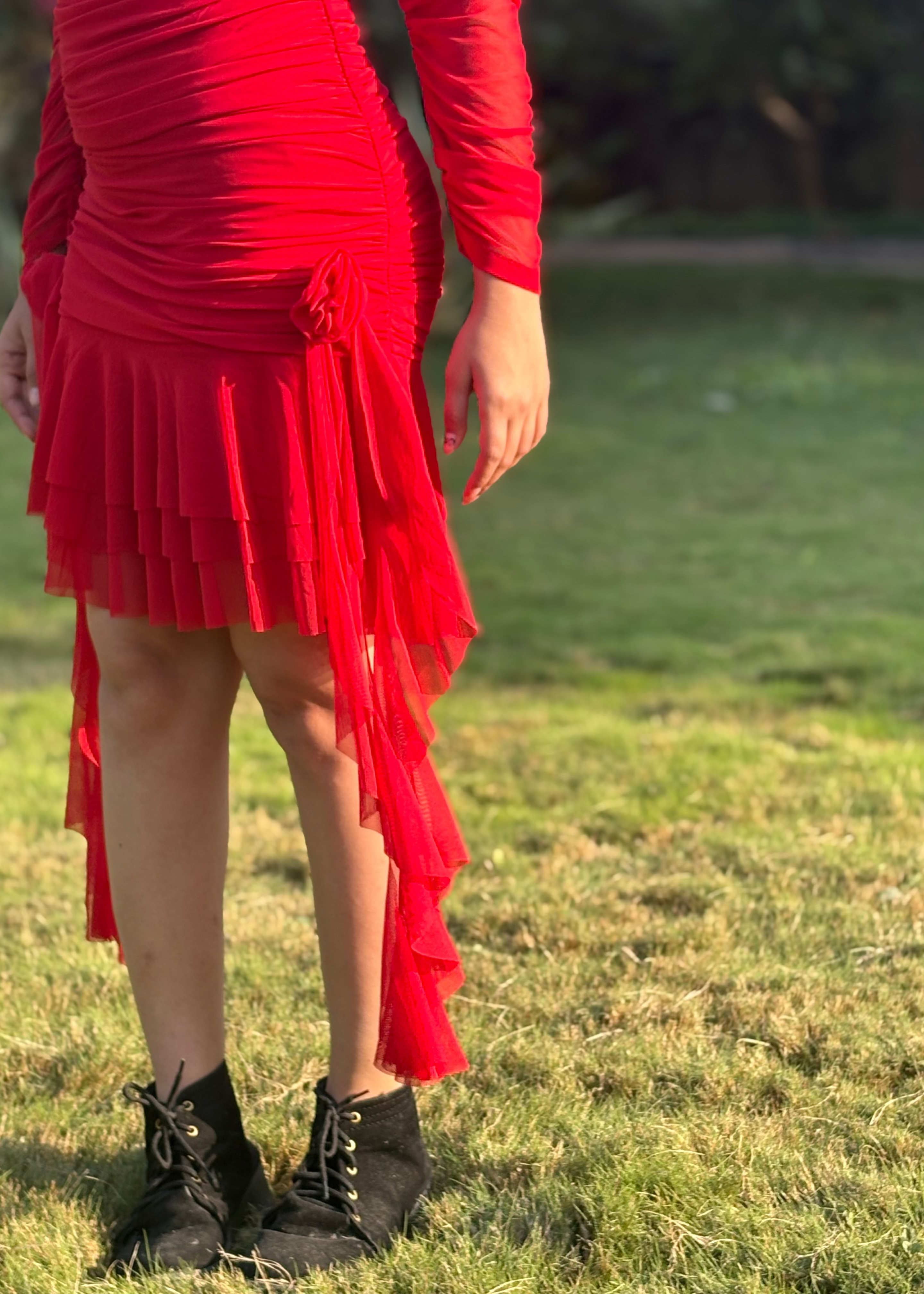 Woman wearing a red ruched dress with pleated hem and black boots, standing on grass