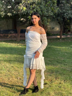 Woman in white off-shoulder ruched dress with ruffle hem standing outdoors on green grass