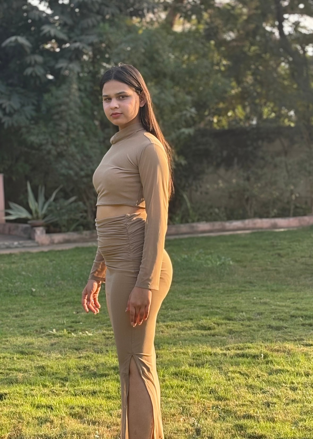 Woman in a tan long-sleeve fitted dress standing outdoors on green grass