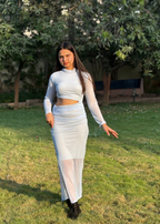 Woman in white sheer long-sleeve cutout dress standing on grass in a sunny outdoor garden
