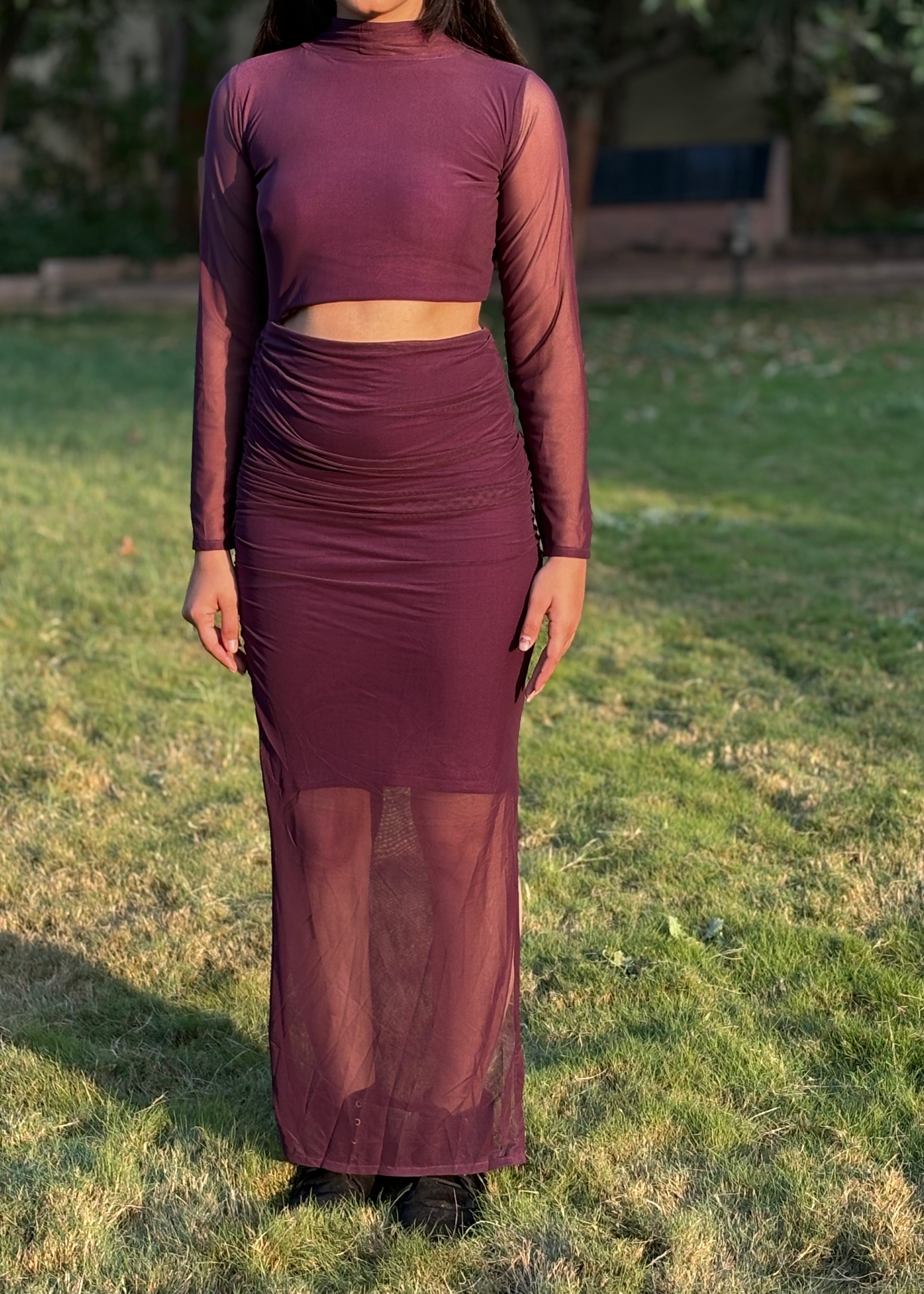 Woman wearing a plum mesh two-piece maxi skirt set with long sleeves in a garden