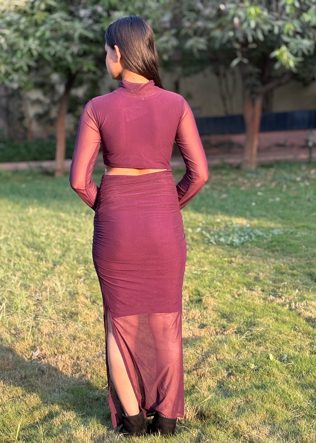 Woman in a sheer plum two-piece mesh dress with long sleeves, standing outdoors on grass
