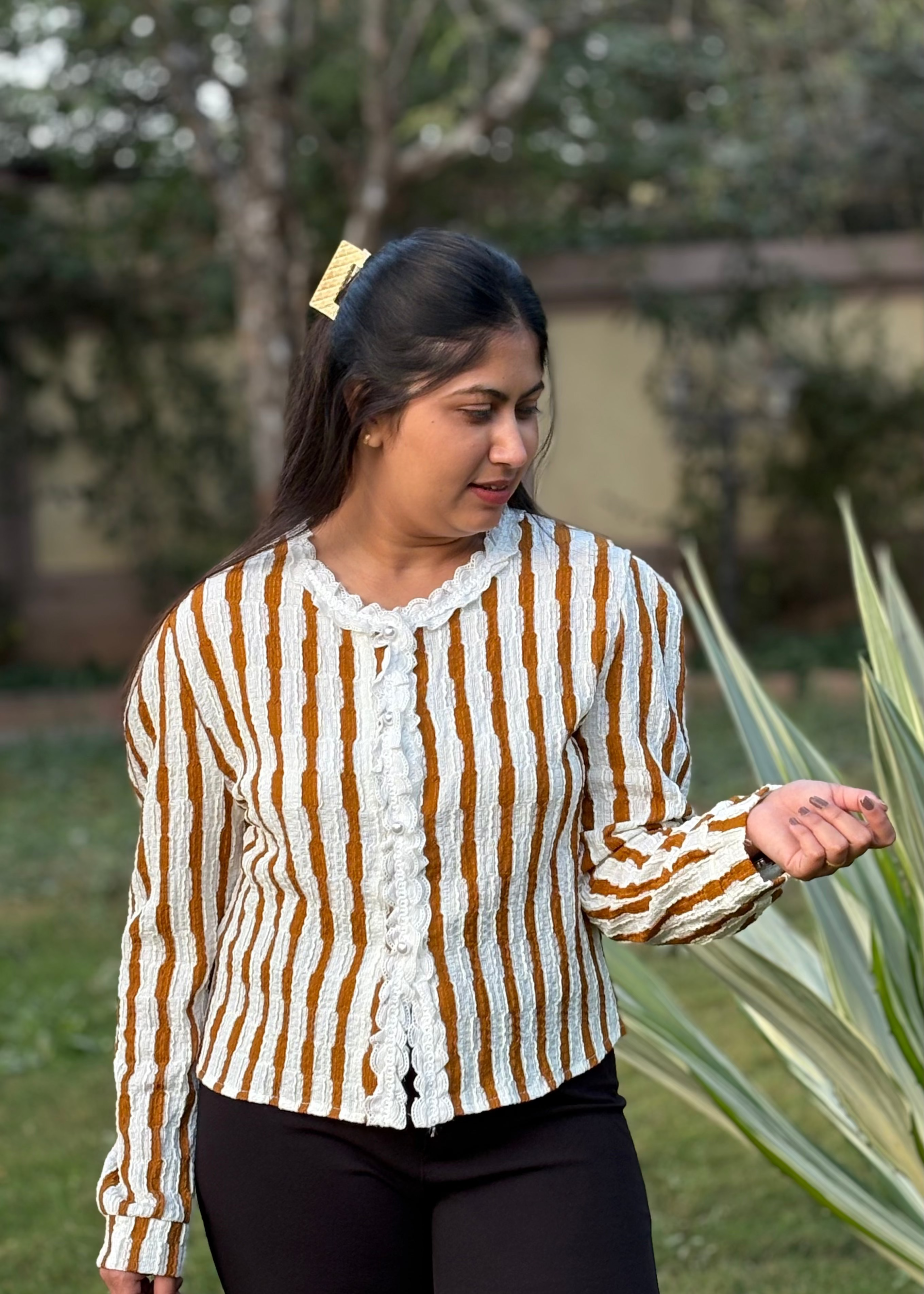Woman outdoors in a textured striped cardigan with ruffled trim and black pants