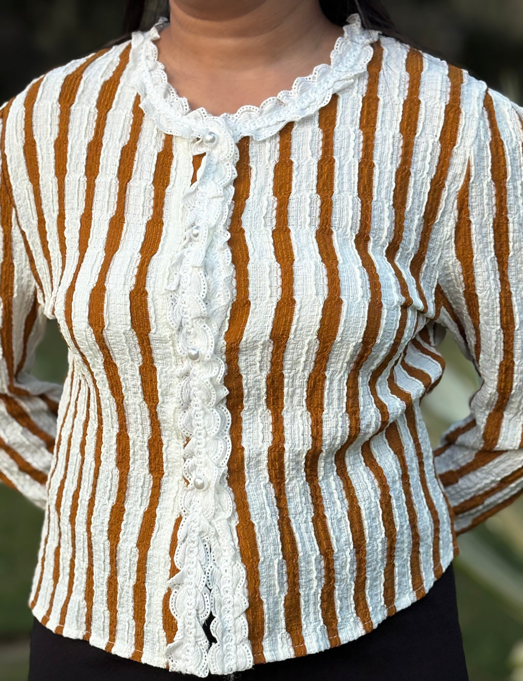 Woman wearing textured long sleeve top with white and brown vertical stripes and lace trim