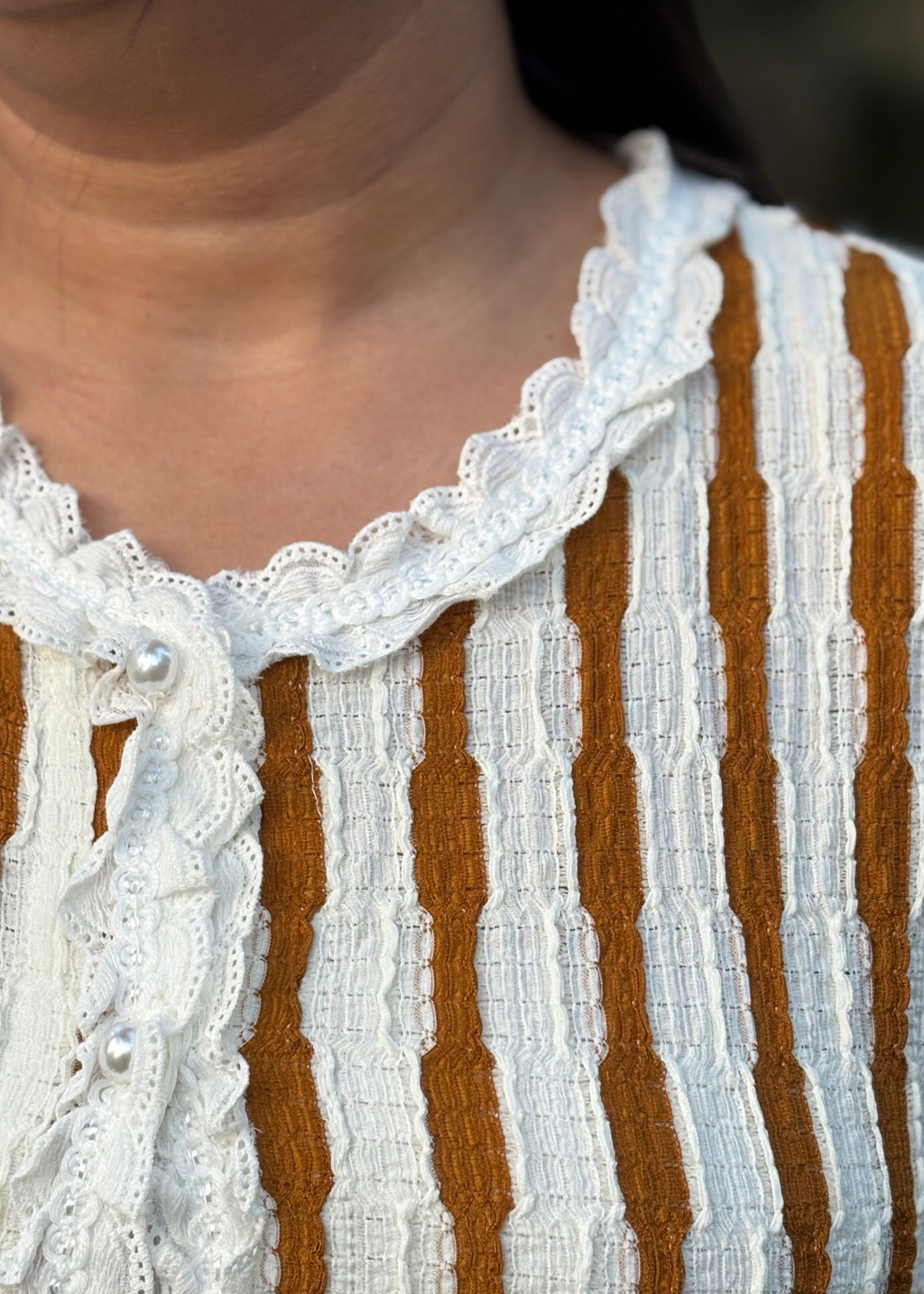 Close-up of a textured blouse with white lace collar, pearl details, and brown-white vertical stripes