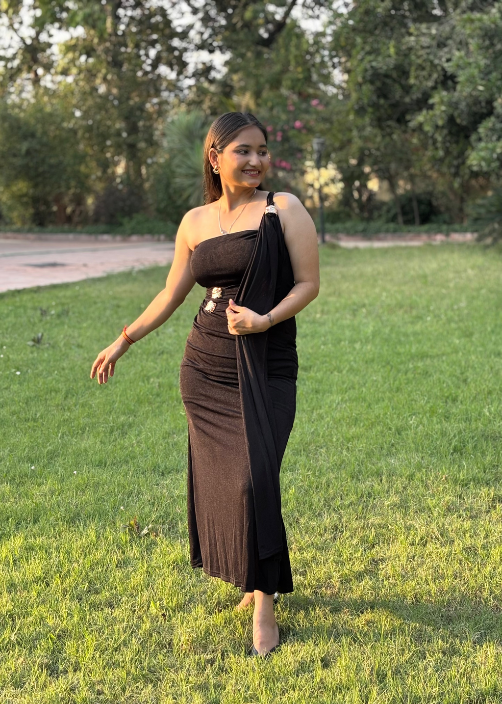 Woman wearing an elegant black one-shoulder dress with silver accents in a garden
