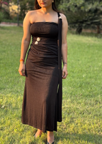 Woman wearing a black one-shoulder dress with gold accents standing outdoors on grass