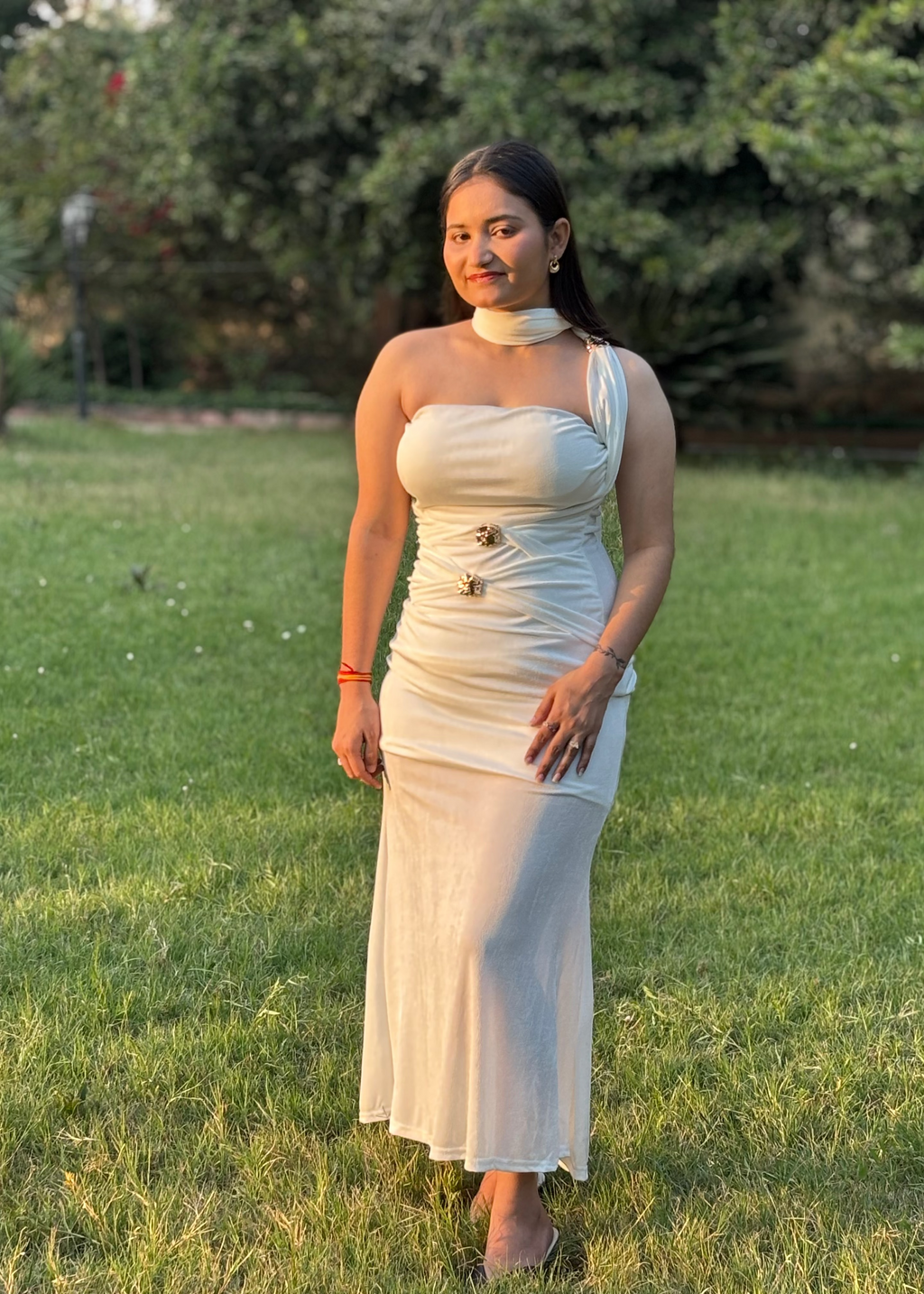 Woman in an elegant ivory strapless gown with gold accents standing on grass outdoors