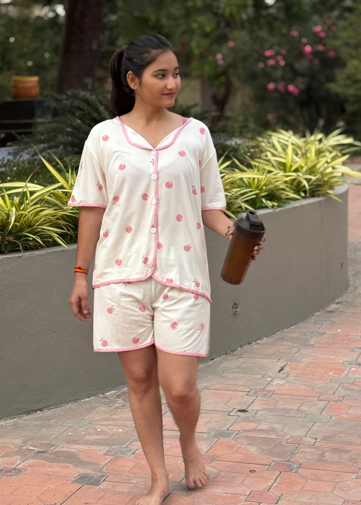 Woman in white and pink polka dot pajama set walking outdoors holding a shaker bottle