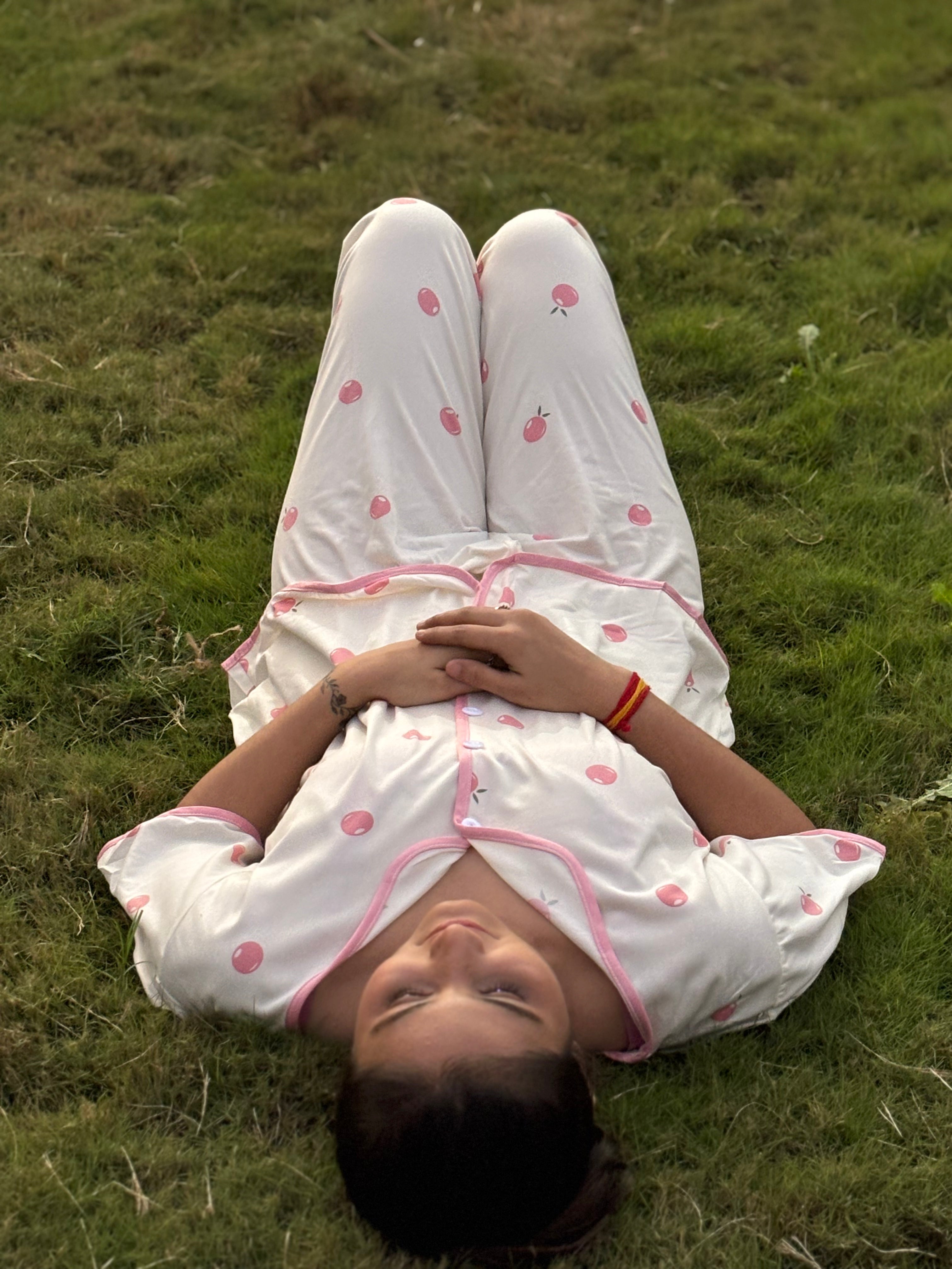 Woman lying on grass wearing white pajamas with pink polka dots and trim