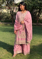 Woman wearing pink embroidered ethnic suit outdoors on grass, traditional festive attire