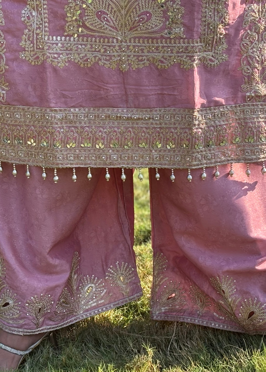 Pink embroidered ethnic outfit with gold threadwork and bead details, outdoor setting