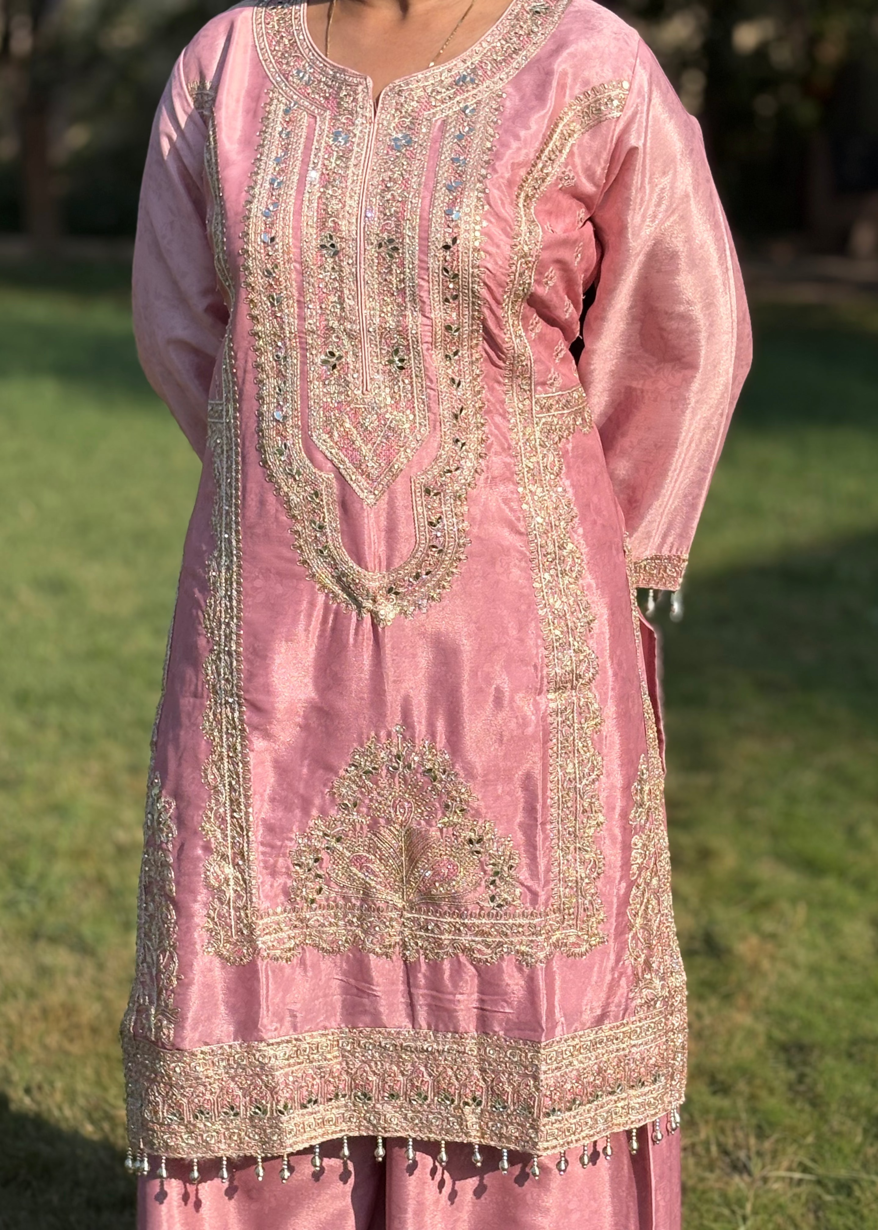 Pink embroidered kurta with gold threadwork and mirror embellishments, worn outdoors