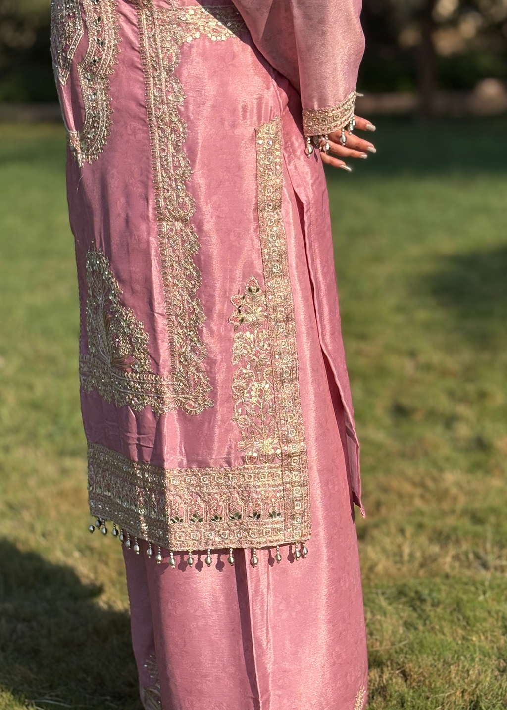 Pink embroidered traditional outfit with gold detailing and beadwork, outdoor setting