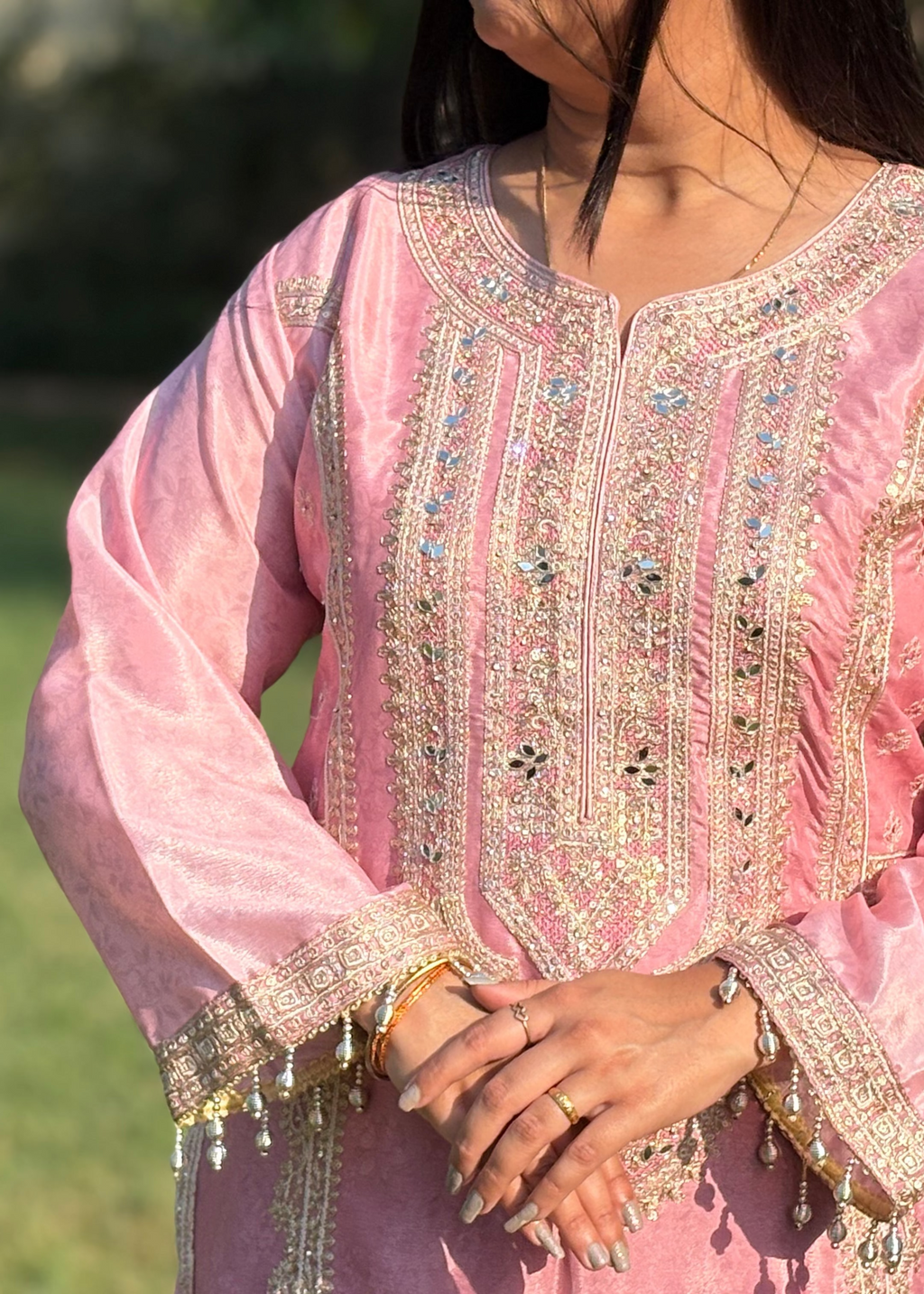 Woman wearing a pink embroidered kurta with gold sequin detailing and beaded cuffs outdoors