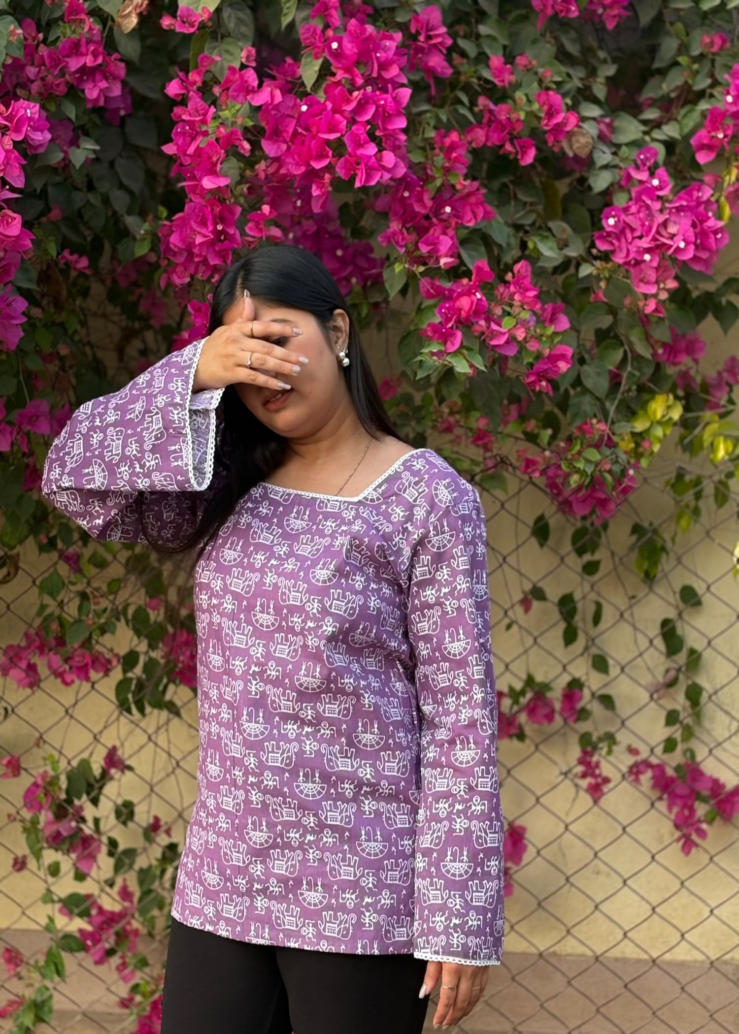 Woman in a purple printed kurti with long sleeves posing by pink bougainvillea flowers