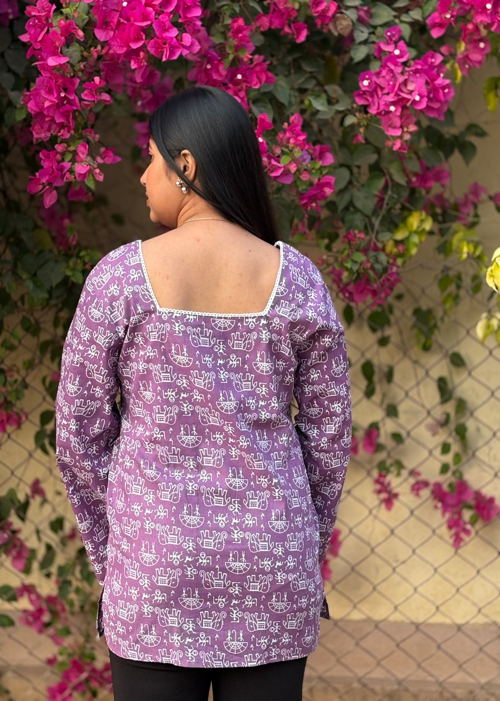 Woman in purple printed tunic with square neckline, standing by pink bougainvillea flowers