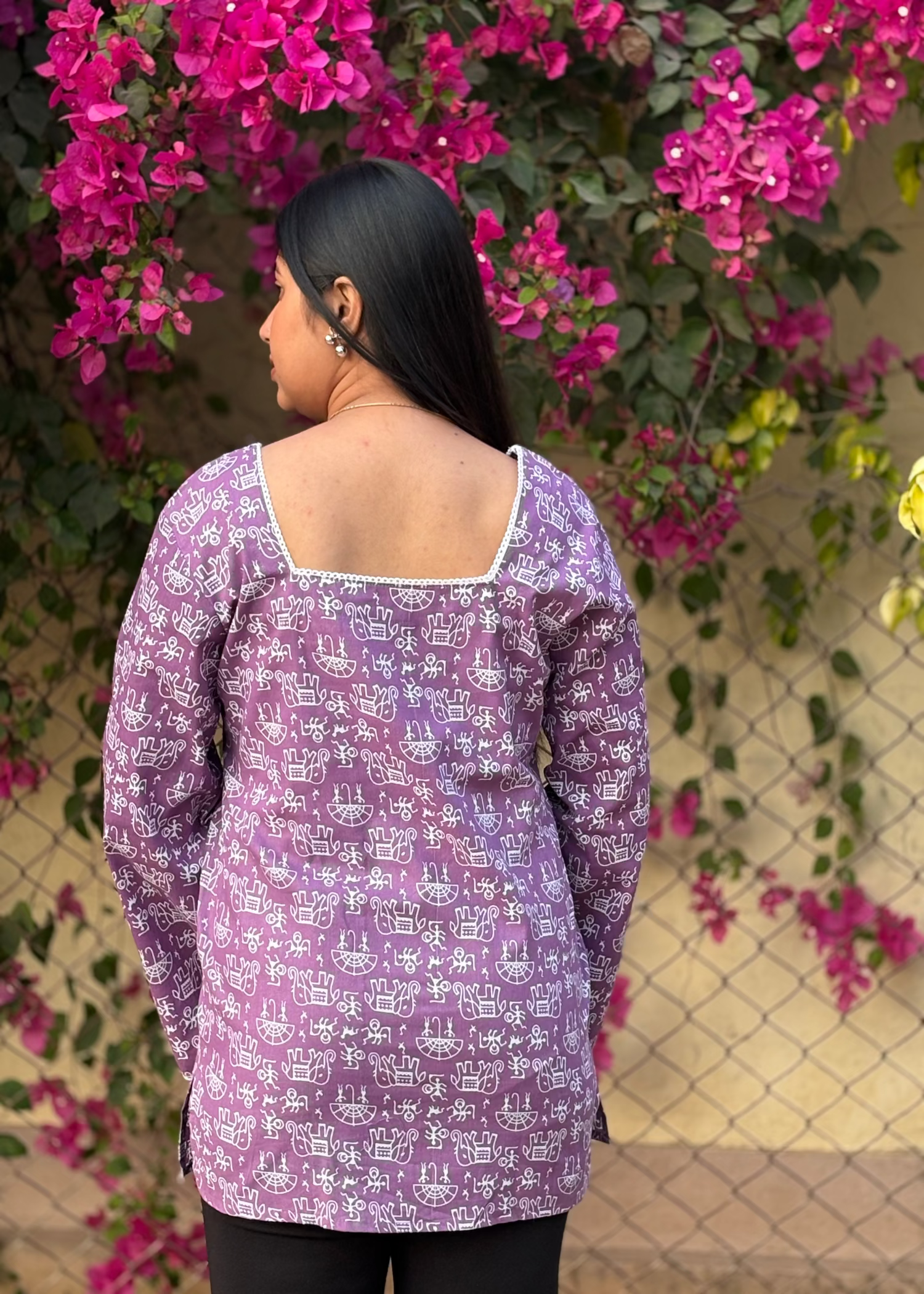 Woman in purple printed tunic with square neckline, standing by pink bougainvillea flowers