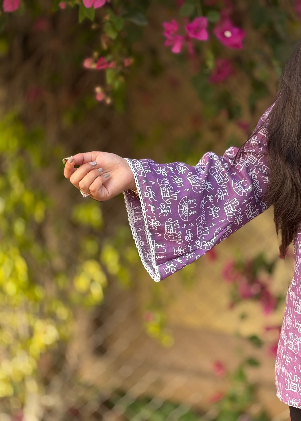 Woman in purple printed kurta with flared sleeve and white lace, holding a flower outdoors